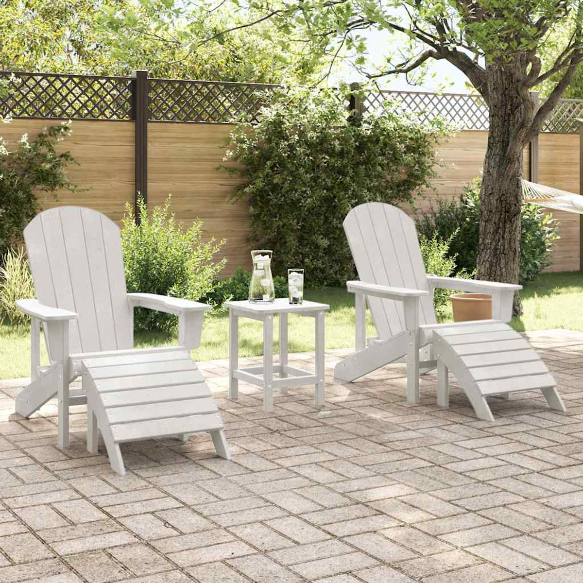 Weiße Adirondack-Stühle und Fußstützen auf einer Terrasse, kleiner Tisch mit Getränken. Hintergrund zeigt einen Zaun, Bäume und Grün.