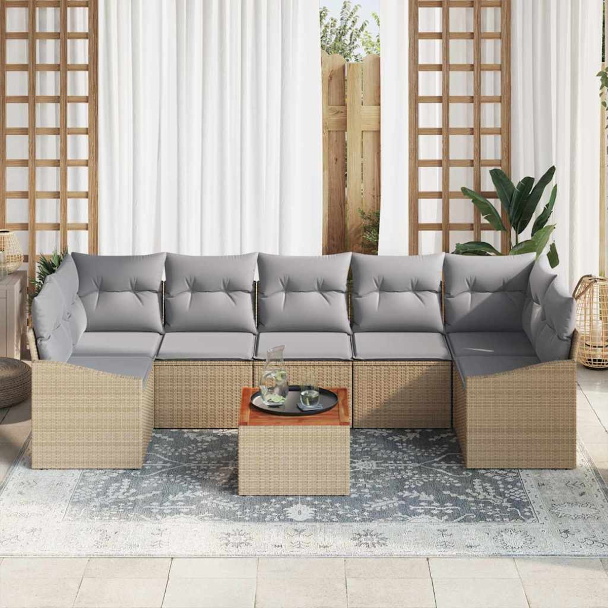 Ein Rattansofa mit grauen Kissen, ein kleiner Tisch mit Getränken und ein gemusterter Teppich auf der Terrasse.