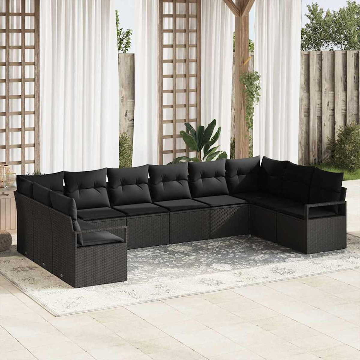 Ein schwarzes Outdoor-Ecksofa auf einem gemusterten Teppich, unter weißen Vorhängen. Hintergrund umfasst Holzgitter, Zaun und Pflanzen.
