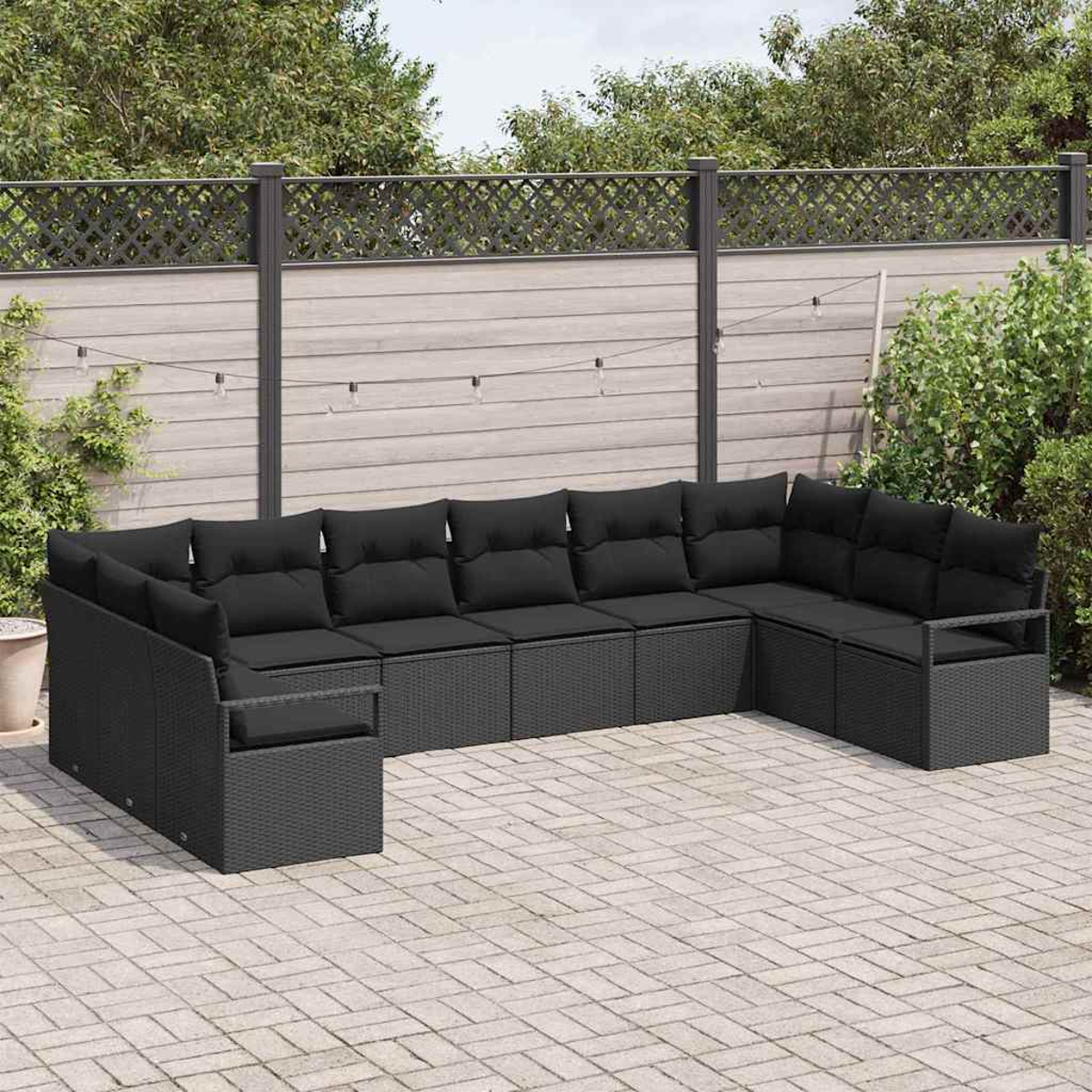 Schwarzes Korbsessel-Sofa mit schwarzen Kissen auf einer Backstein-Terrasse. Im Hintergrund ein Zaun, Pflanzen und eine Lichterkette.