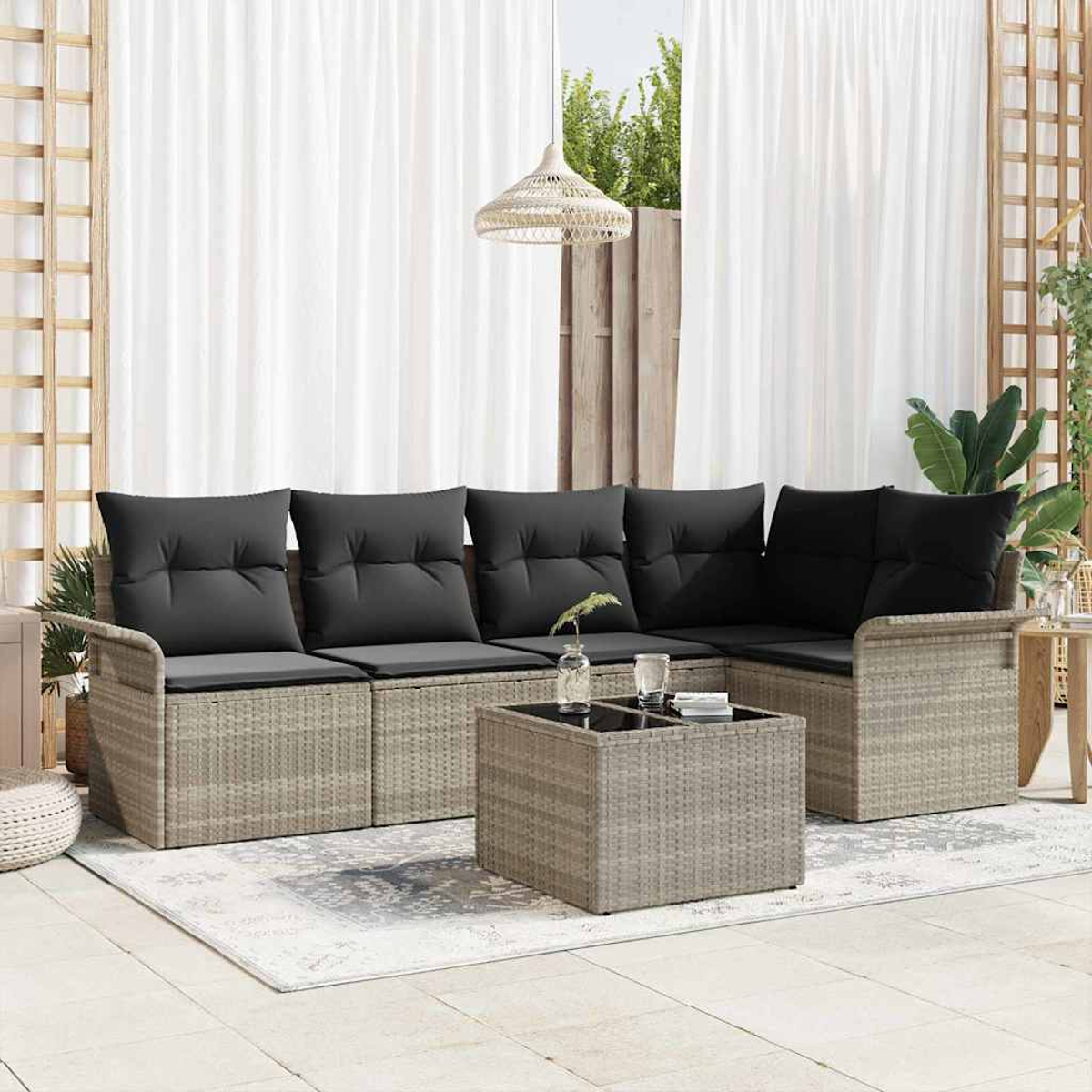 Outdoor-Ecksofa mit schwarzen Kissen, Couchtisch, Teppich und weißen Vorhängen. Im Hintergrund Pflanzen und ein Holzgitter.