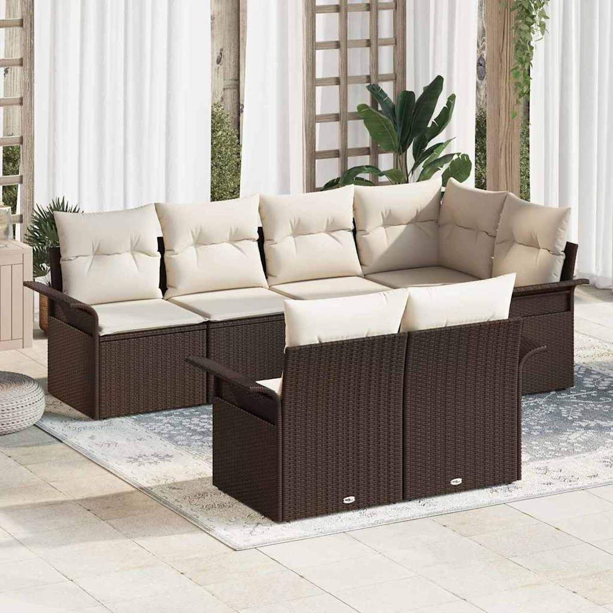 Garten-Sitzgruppe mit braunen Korbflechtrahmen und beigefarbenen Kissen. Auf einem Teppich, mit weißen Vorhängen und Pflanzen im Hintergrund.