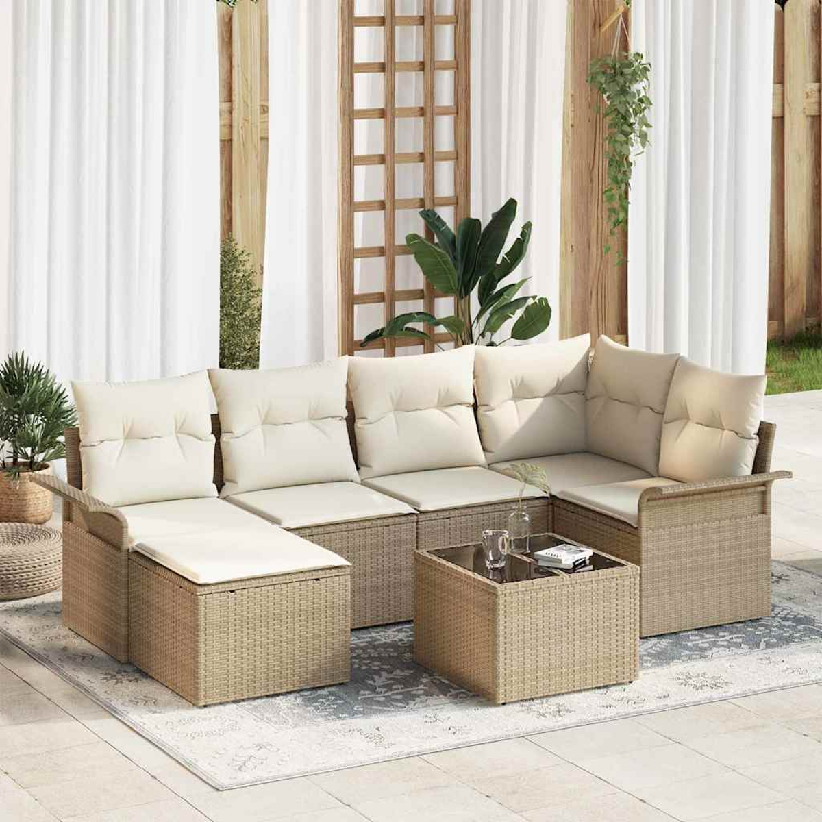 Geflochtenes Outdoor-Ecksofa mit cremefarbenen Kissen und einem kleinen Tisch. Pflanzen und weiße Vorhänge im Hintergrund.