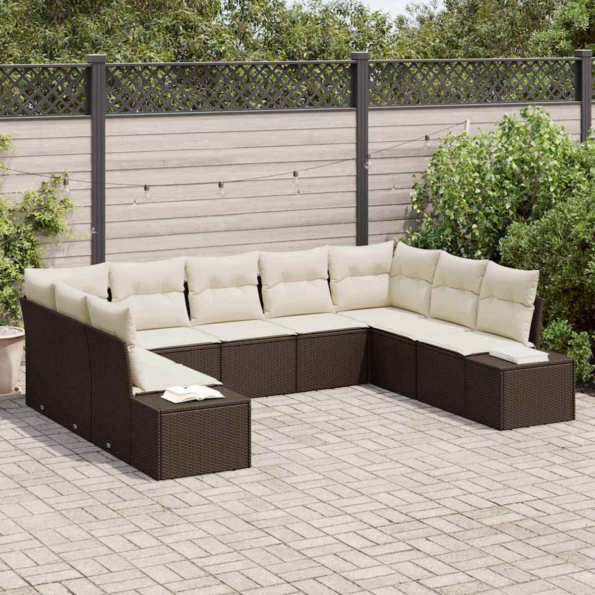 Ein braunes Korbsessel-Sofa mit cremefarbenen Kissen steht auf einer Terrasse. Ein Zaun und Pflanzen bilden den Hintergrund.