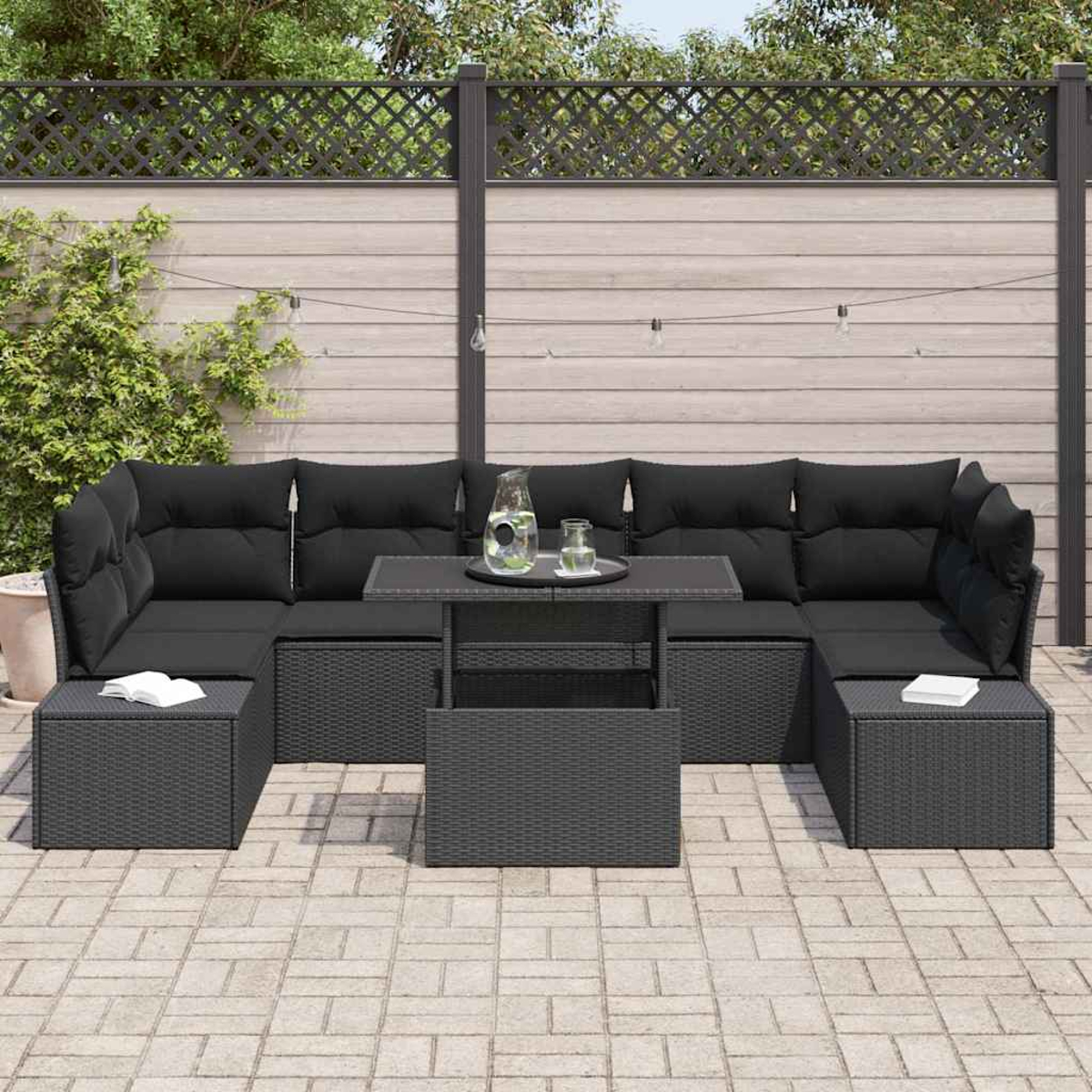 Garten-Sitzgruppe mit schwarzen Kissen und einem Tisch. Auf dem Tisch stehen ein Krug und Gläser. Der Hintergrund zeigt einen Zaun.
