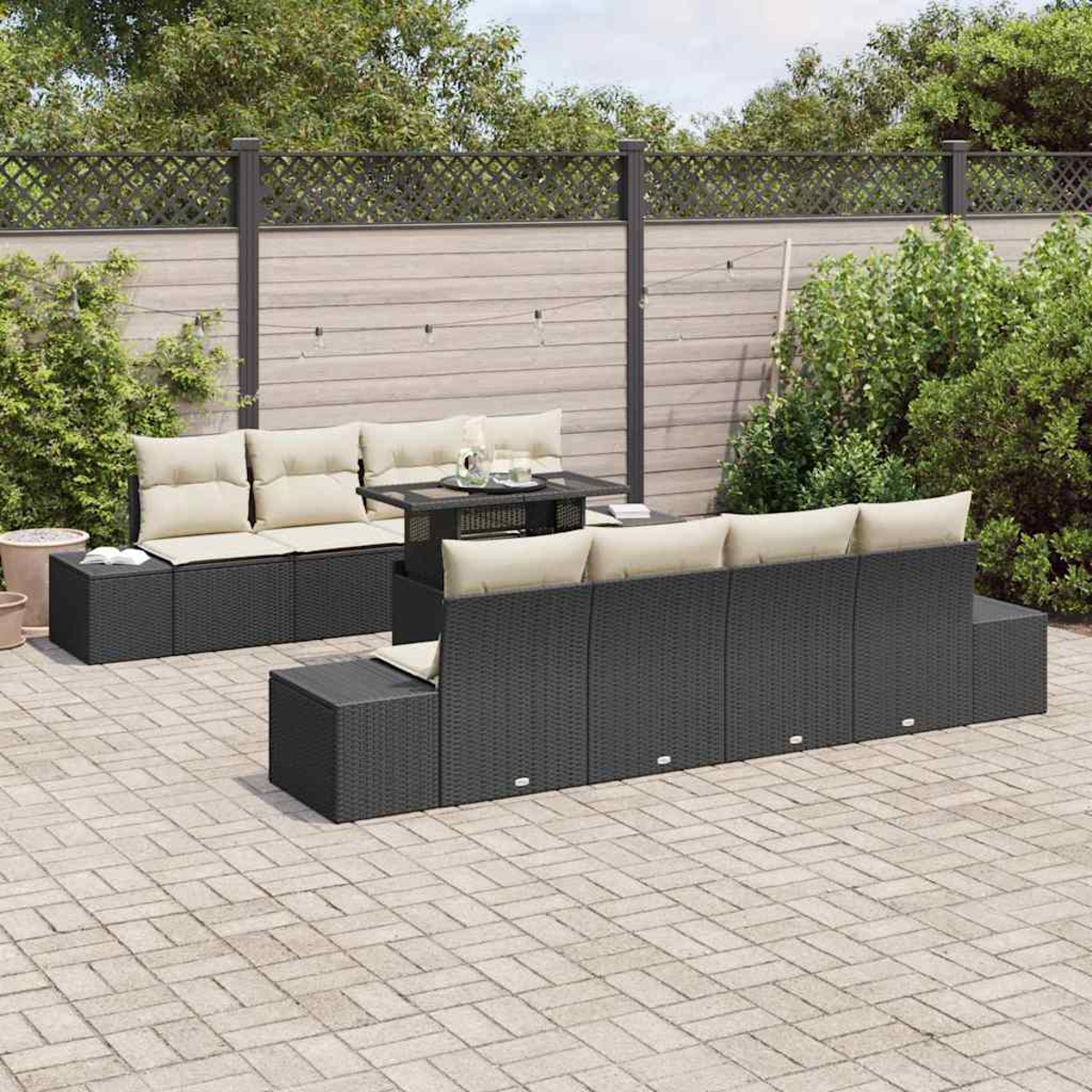 Juego de patio al aire libre con muebles de mimbre negro, cojines beige y una mesa pequeña. La escena incluye una valla y follaje.