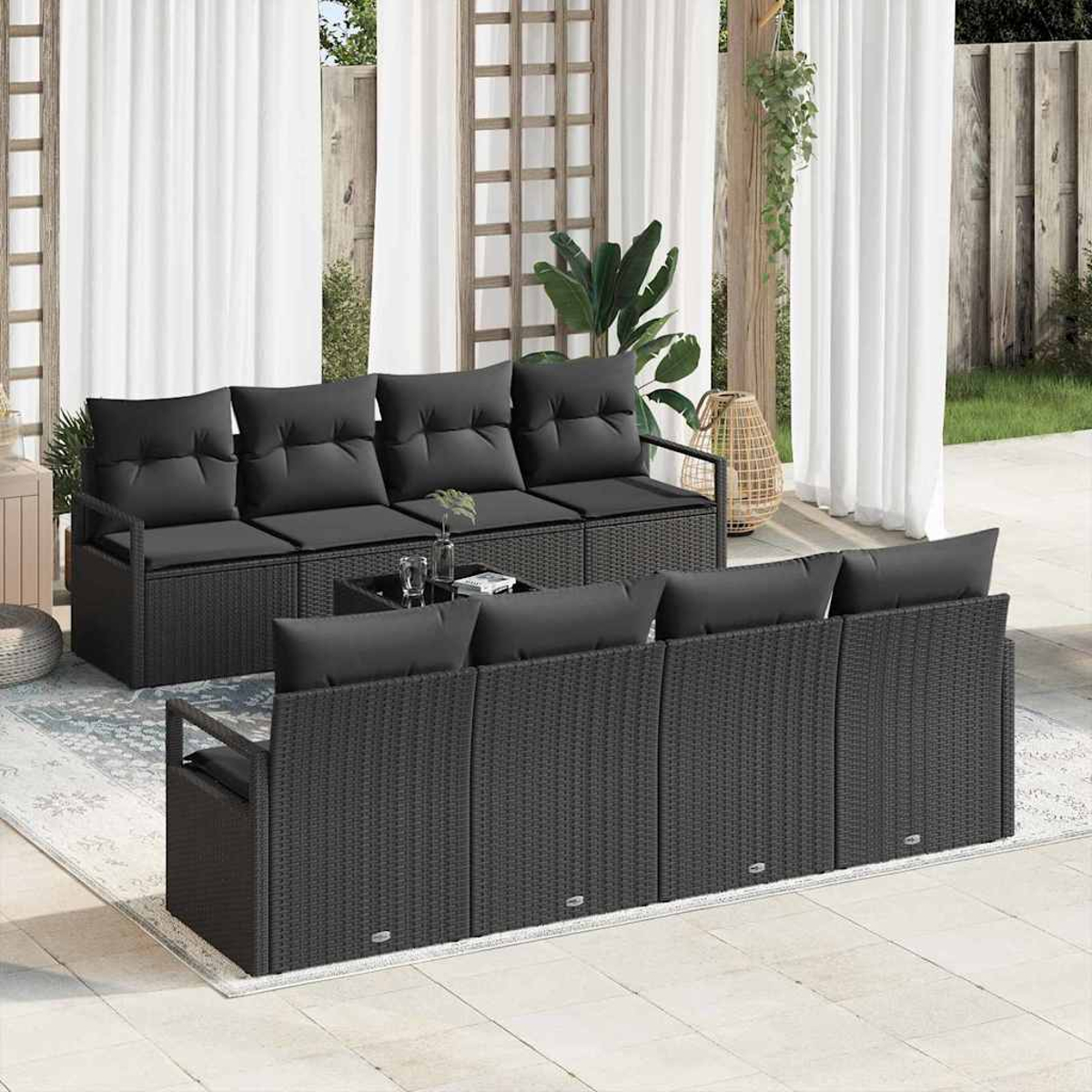 Terrassen-Set: schwarze Korbsessel, Kissen und Couchtisch. Weiße Vorhänge und Pflanzen im Hintergrund. Sitzbereich im Freien.
