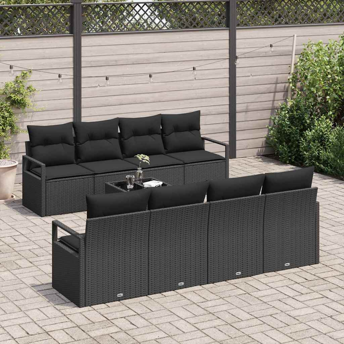 Outdoor-Terrassenset mit schwarzen Kissen, einem Couchtisch und einem Holzzaun im Hintergrund. Die Umgebung ist eine Ziegelterrasse.
