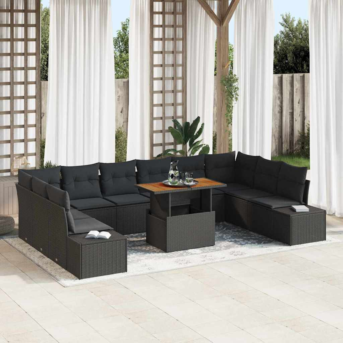 Outdoor-Terrassenset mit schwarzen Korbmöbeln, Kissen und einem Tisch mit Holzplatte. Weiße Vorhänge und Grün im Hintergrund.