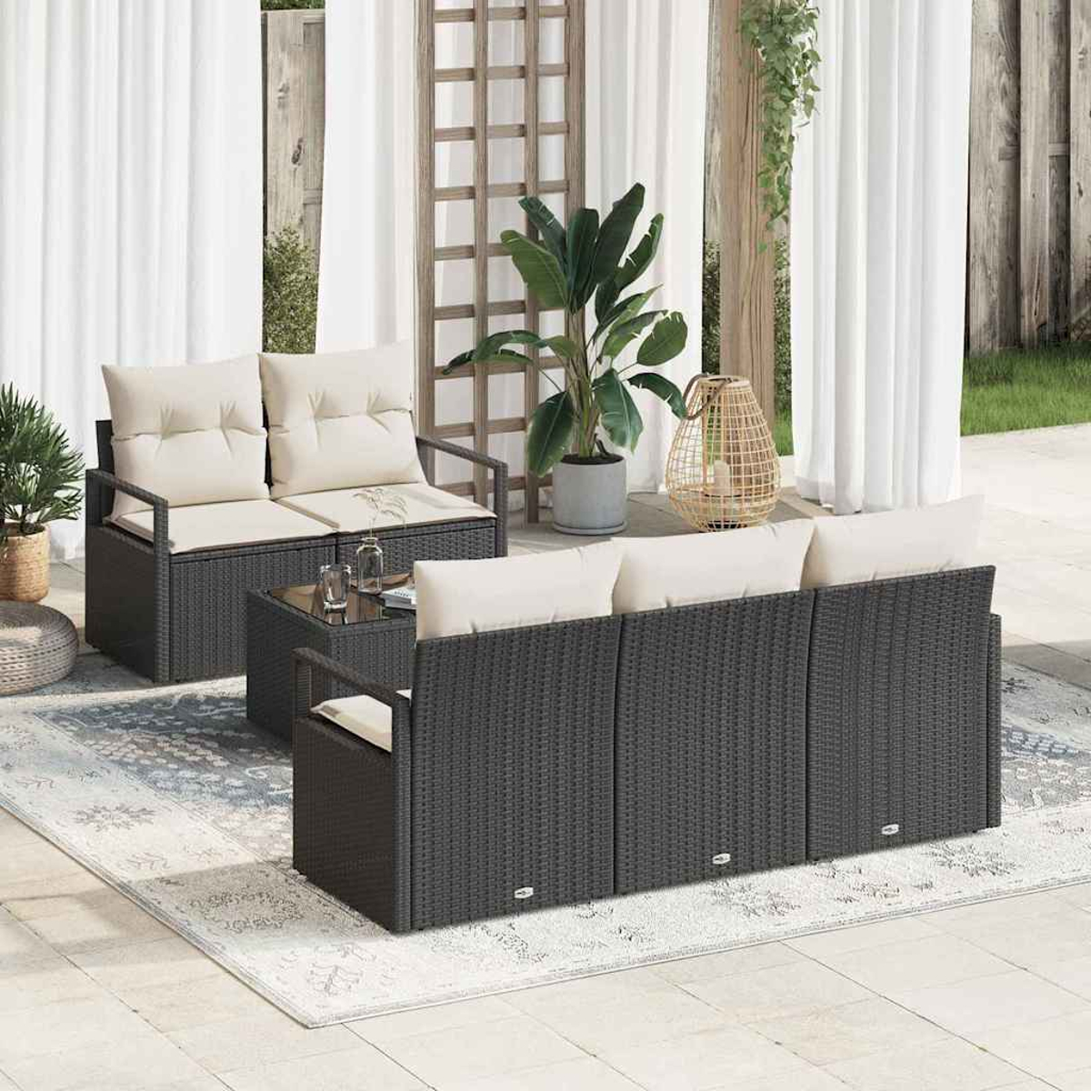 Juego de muebles de patio con sofás de mimbre gris oscuro, cojines beige y una mesa de cristal sobre una alfombra estampada.