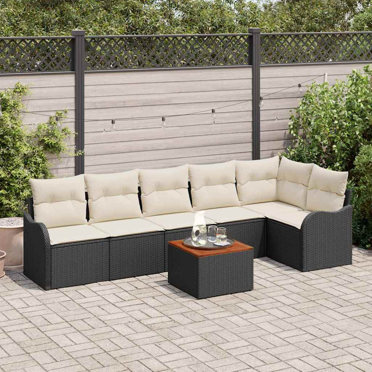 Outdoor-Ecksofa mit cremefarbenen Kissen und einem kleinen Tisch auf einer Backstein-Terrasse. Ein Zaun und Grün sind im Hintergrund.