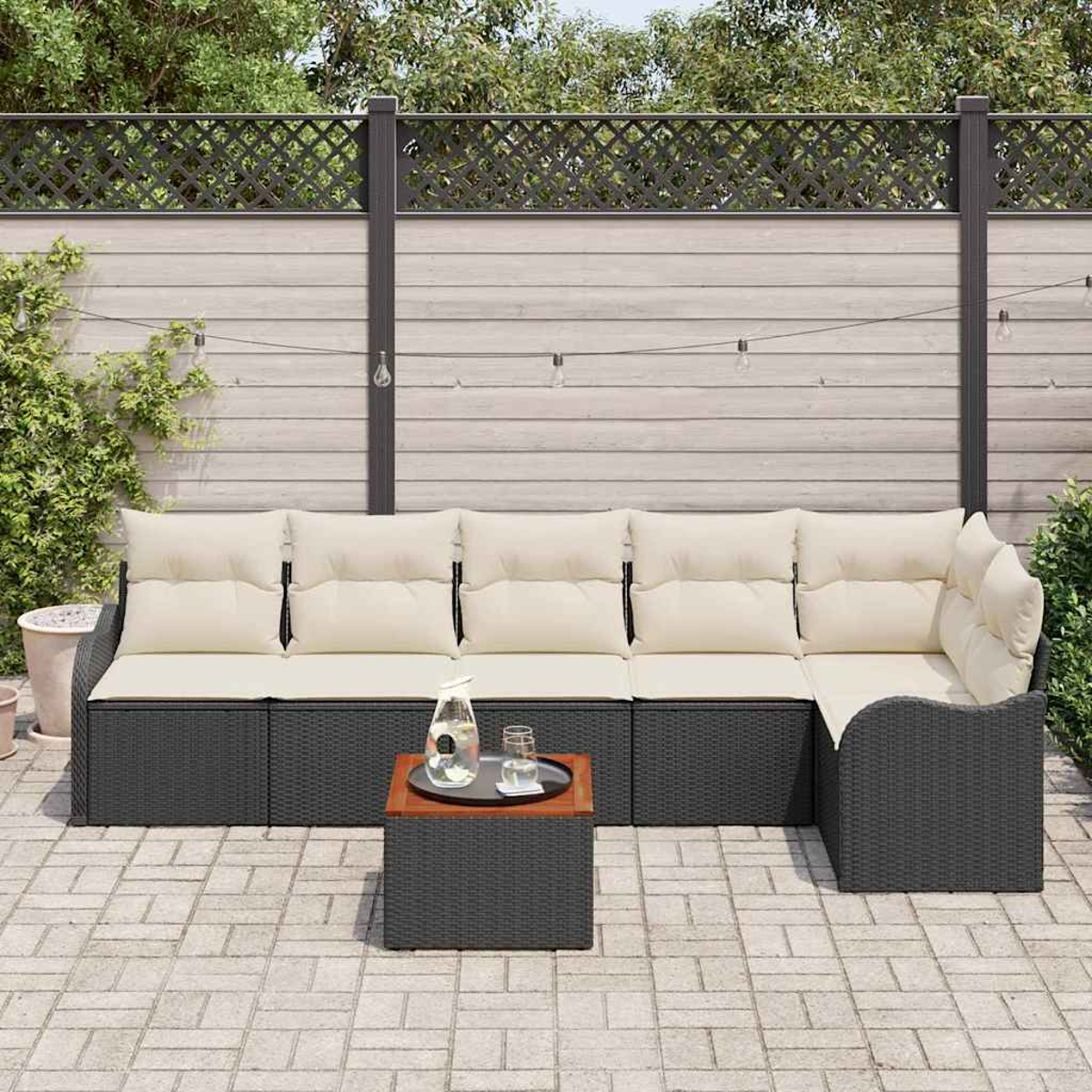 Garten-Sitzgruppe mit cremefarbenen Kissen und einem kleinen Tisch mit Getränken. Im Hintergrund ein Zaun und Grün.