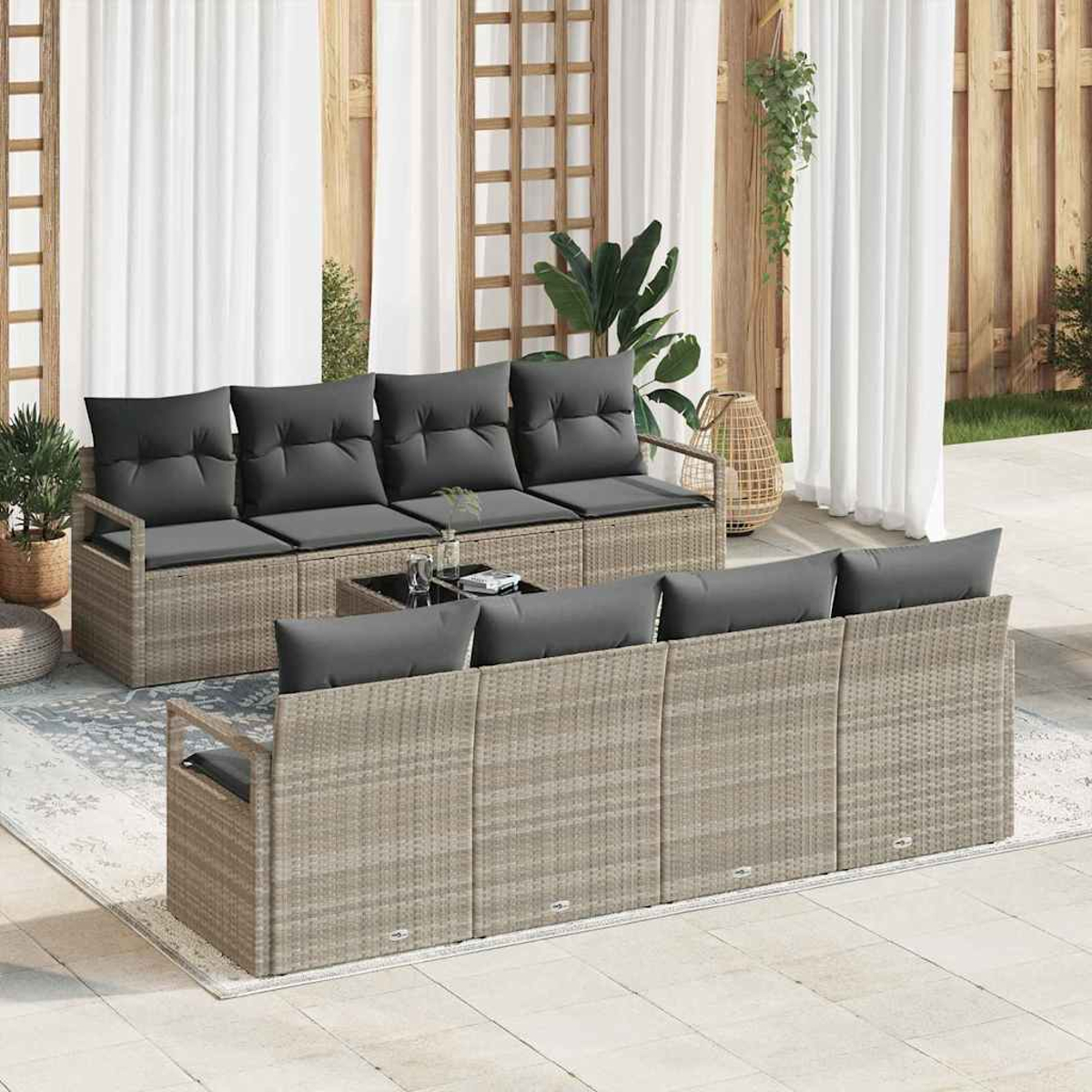 Terrassenmöbel-Set mit grauen Kissen auf Korbmöbeln. Enthält Tisch, Pflanzen und weiße Vorhänge.