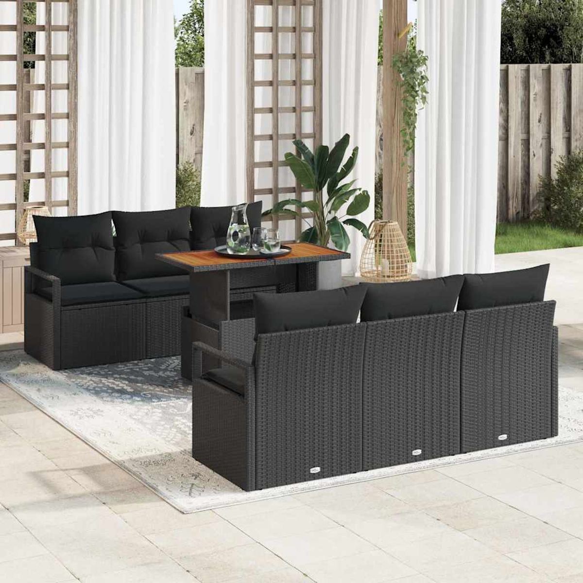 Gartenmöbel-Set. Schwarze Korbsessel und Tisch mit schwarzen Kissen. Weiße Vorhänge und Grün im Hintergrund.