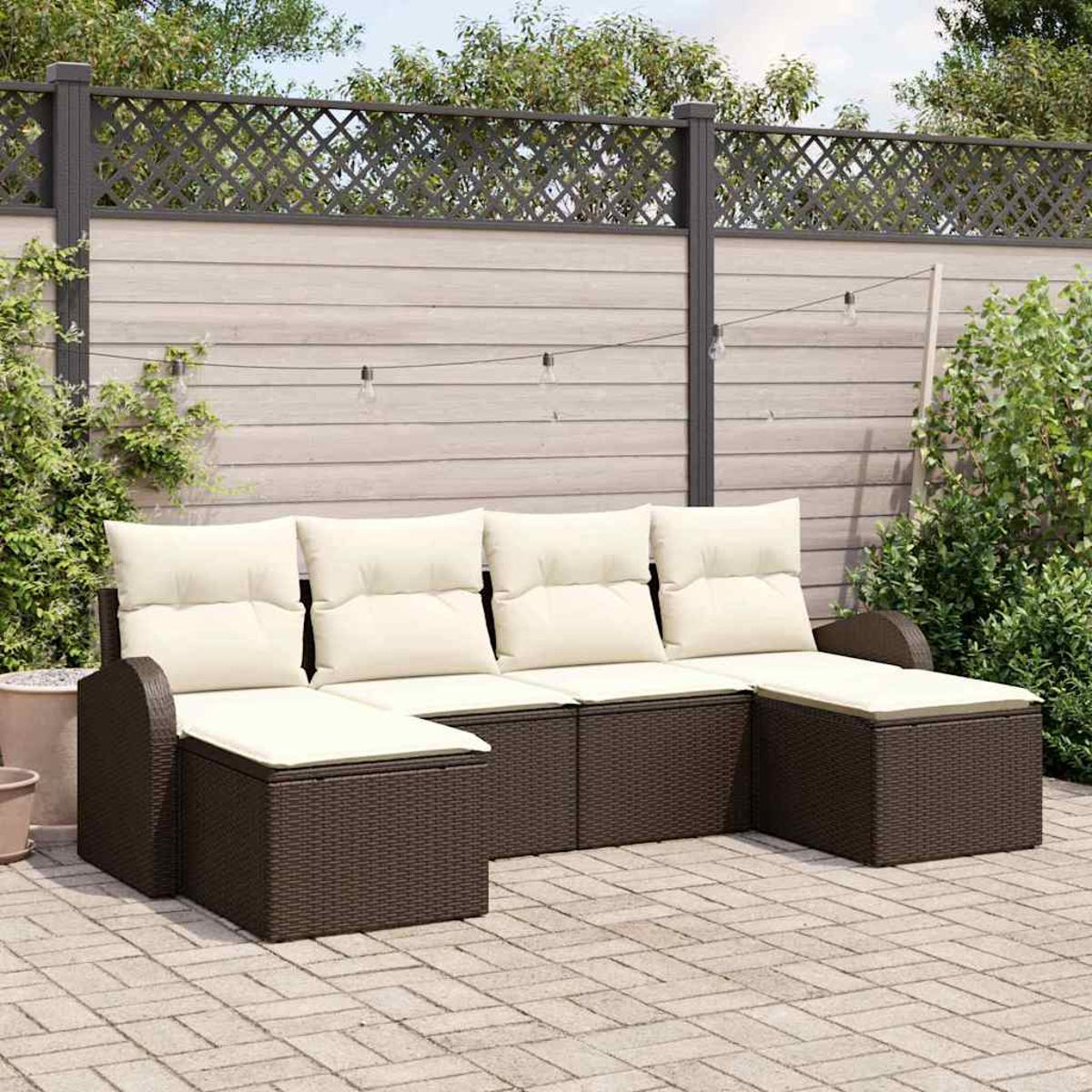 Braunes Outdoor-Korbmöbel mit cremefarbenen Kissen auf einer Ziegelterrasse. Ein Holzzaun und Grün im Hintergrund.