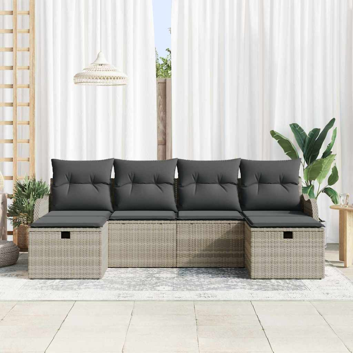 Ein helles Rattan-Sofa mit grauen Kissen steht vor weißen Vorhängen. Eine Pflanze und eine Lampe befinden sich neben dem Sofa.