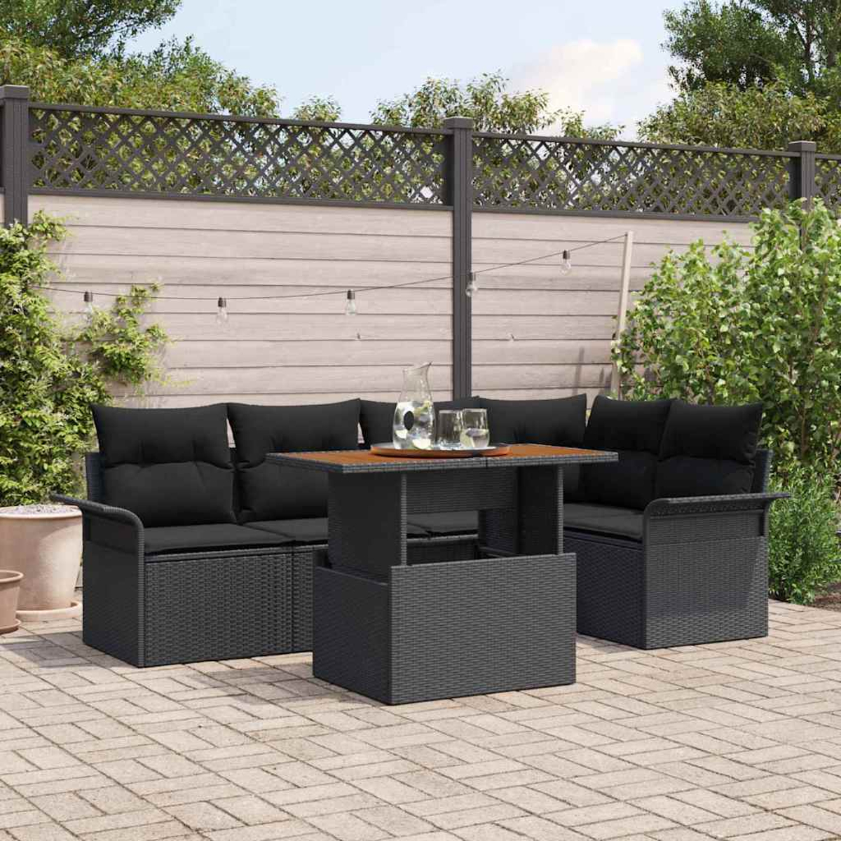 Terrassenmöbel-Set mit dunkelgrauem Korbsessel und Stühlen, Tisch und Holzplatte. Im Hintergrund befindet sich ein Zaun.