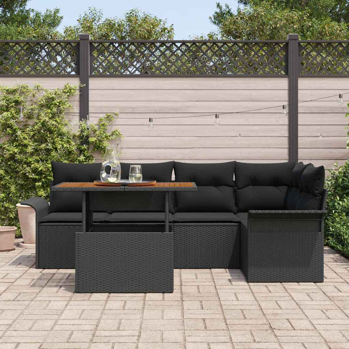 Gartenlounge-Set mit schwarzen Kissen und einem Holztisch. Hintergrund: Zaun, Pflanzen und Lichterketten.