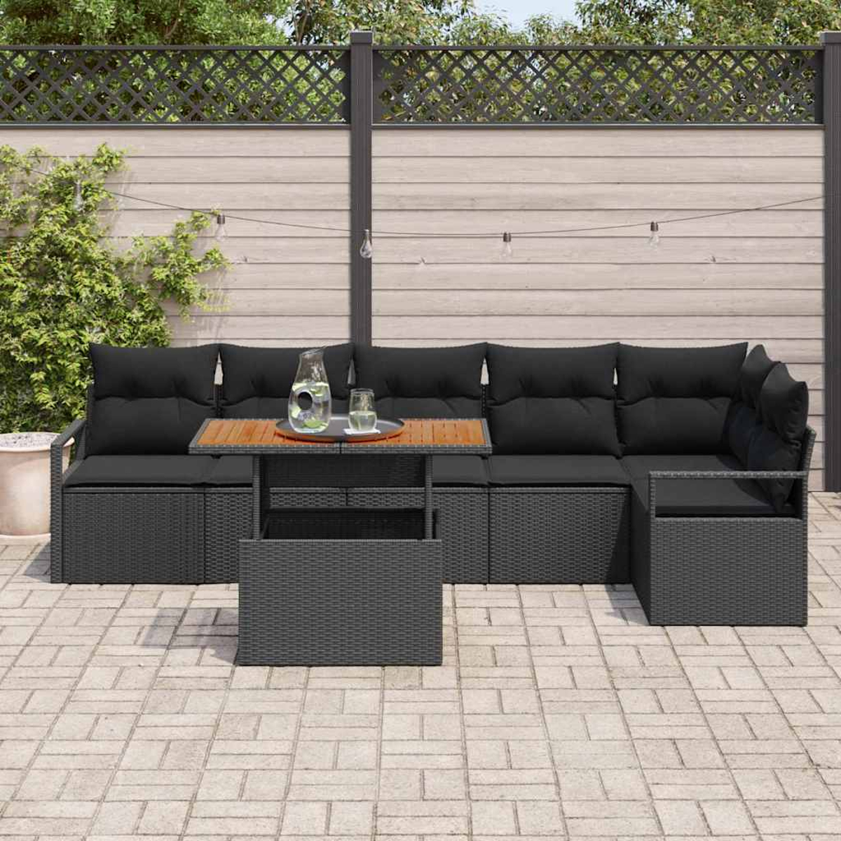 Outdoor-Ecksofa mit schwarzen Kissen und einem Holztisch. Auf dem Tisch stehen ein Glaskrug und ein Glas. Die Terrasse ist gepflastert.