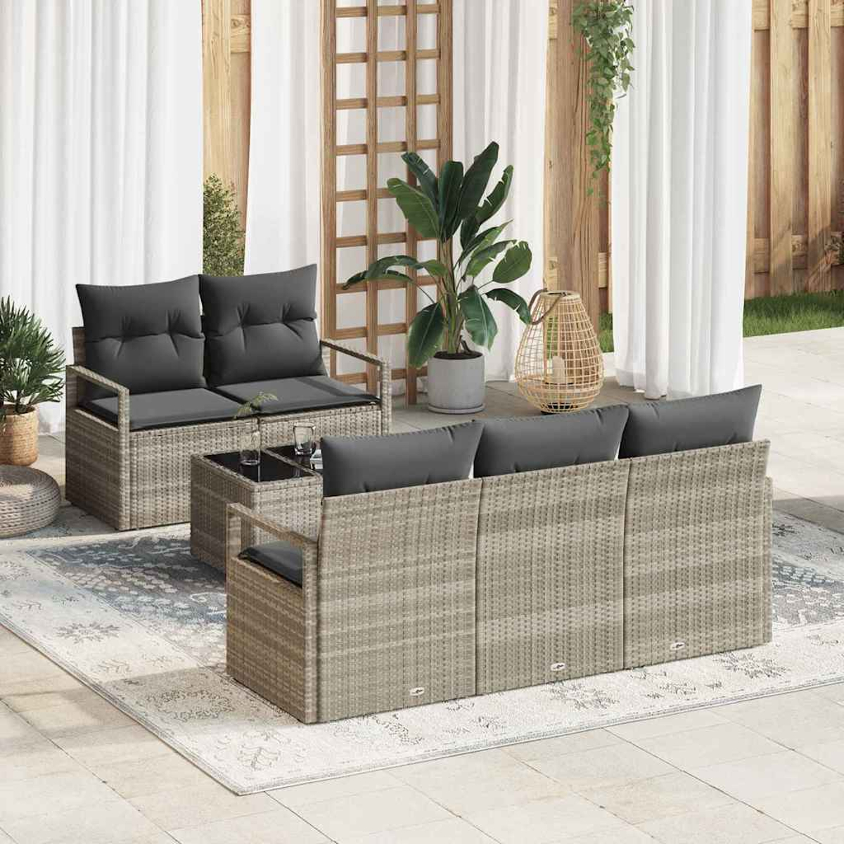 Außenszene mit Rattan-Sofagarnitur, Kissen, Glastisch, Teppich, Pflanzen, Vorhängen und einem Holzgitter.