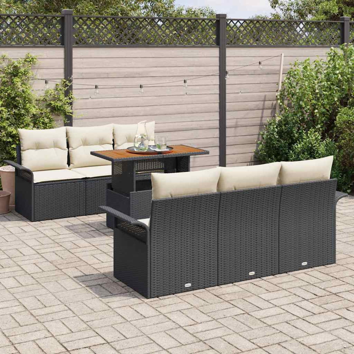 Terrassenmöbel-Set mit schwarzem Korbmöbeln, beigen Kissen und einem Holztisch. Auf einer Backsteinterrasse mit Holzzaun.