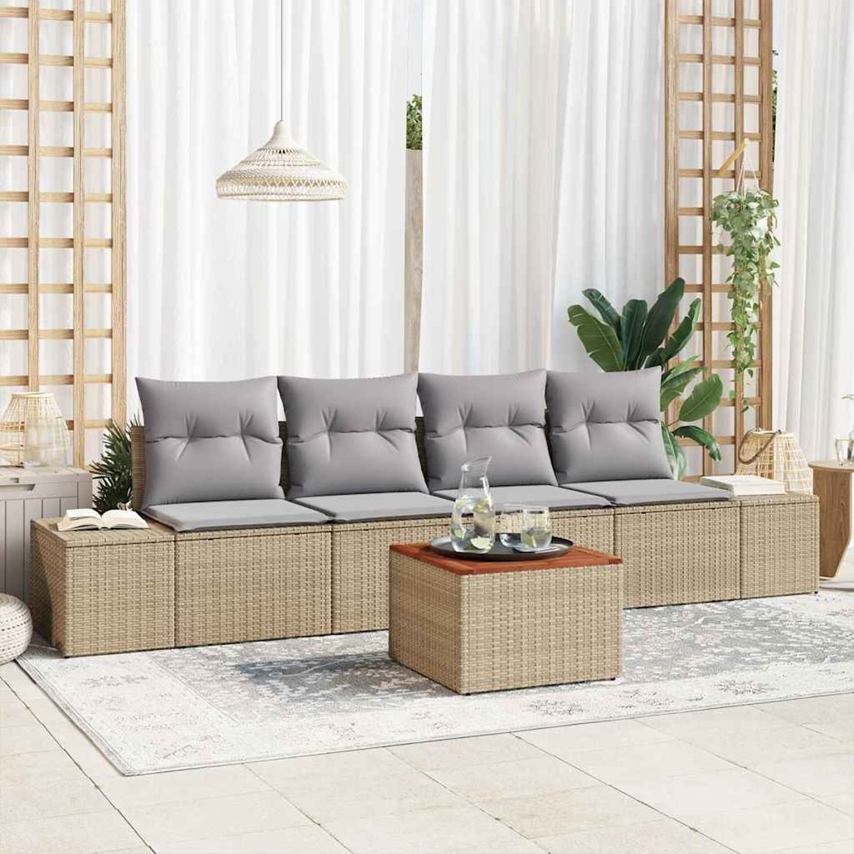 Outdoor-Sitzbereich mit gewebten Möbeln, grauen Kissen, einem Couchtisch und weißen Vorhängen. Dekorative Pflanzen und ein Teppich sind vorhanden.