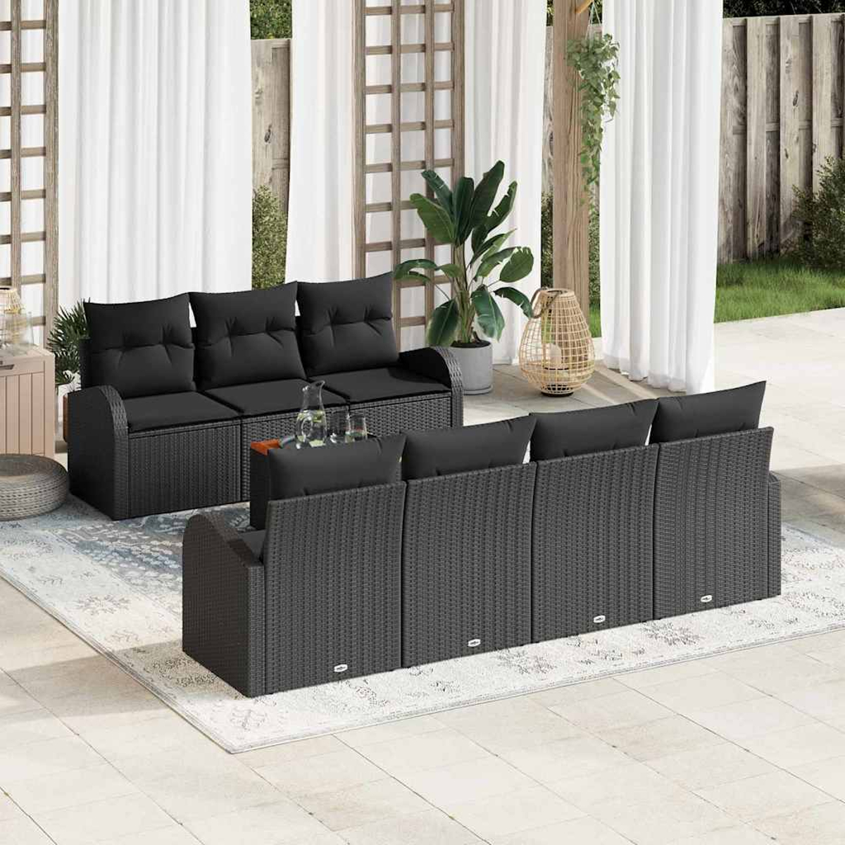 Garten-Terrassenset mit schwarzen Korbsesseln, Kissen und einem Tisch. Weiße Vorhänge, Pflanzen und ein Teppich vervollständigen die Szene.