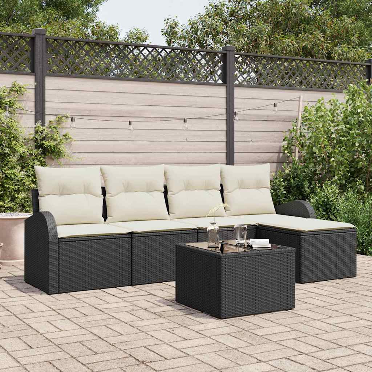 Terrassen-Set im Freien. Dunkles Korbmöbel-Sofa mit cremefarbenen Kissen, Couchtisch und Holzzaun-Hintergrund mit grünem Laub.
