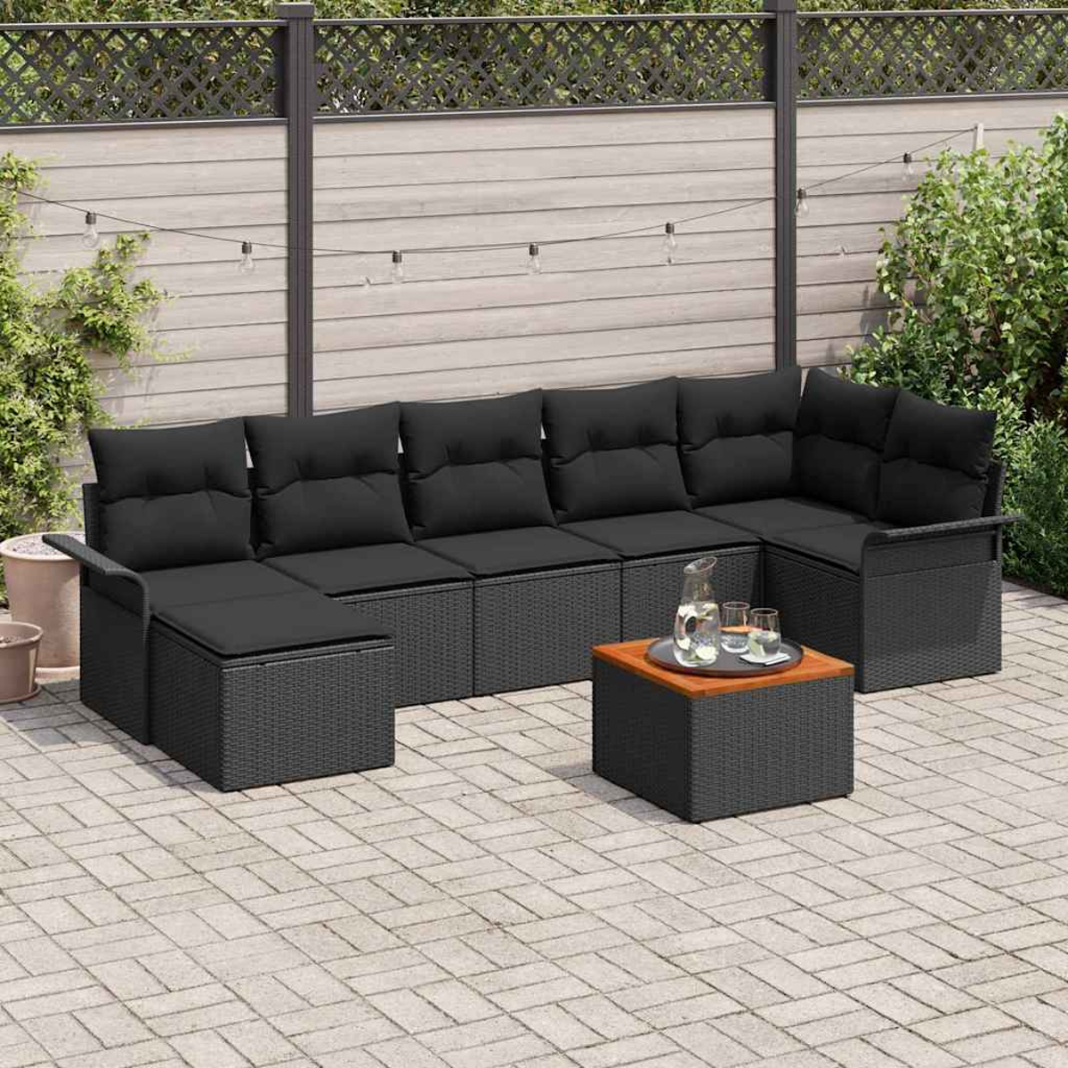 Outdoor-Ecksofa mit schwarzen Kissen und einem kleinen Tisch. Im Hintergrund ein Holzzaun und Grün. Getränke auf dem Tisch.