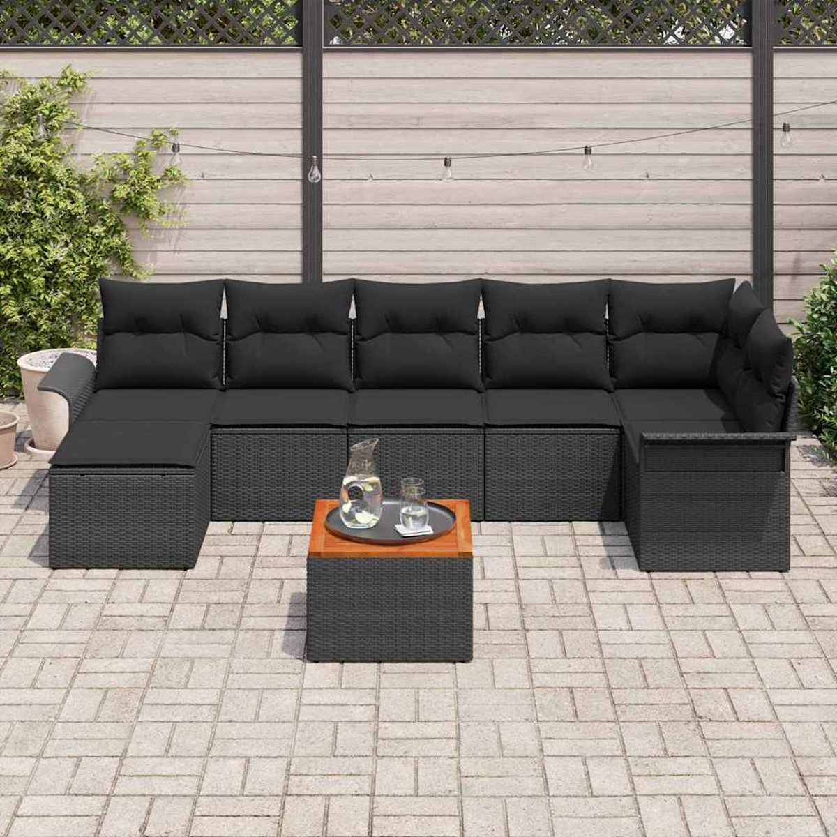 Garten-Terrassenset mit schwarzen Kissen, einem kleinen Tisch mit einem Glas Wasser und einem Krug auf einer Steinterrasse.