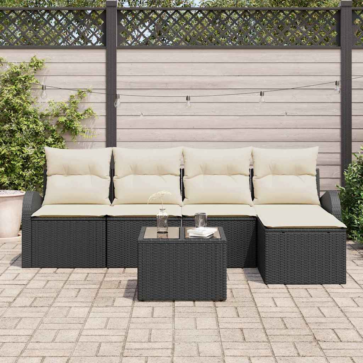 Outdoor-Ecksofa mit cremefarbenen Kissen und einem kleinen Tisch. Im Hintergrund ein Holzzaun und Grünpflanzen.