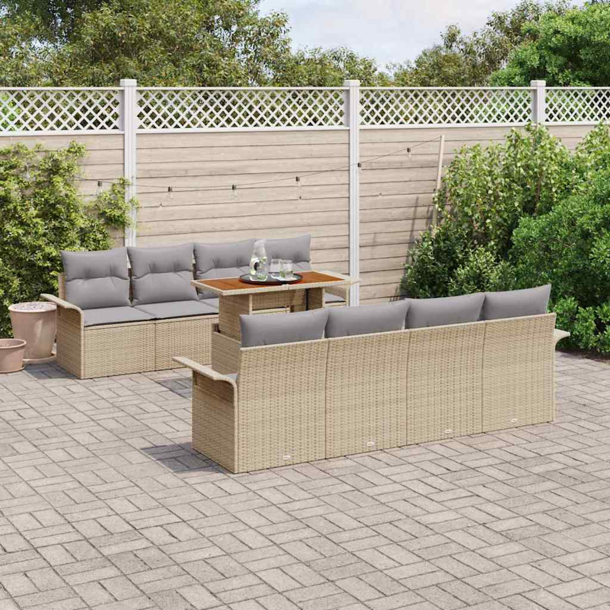 Garten-Terrassenset mit Korbsitzgruppen, grauen Kissen und einem Holztisch, auf einer Backstein-Terrasse, mit Zaun und Pflanzen im Hintergrund.