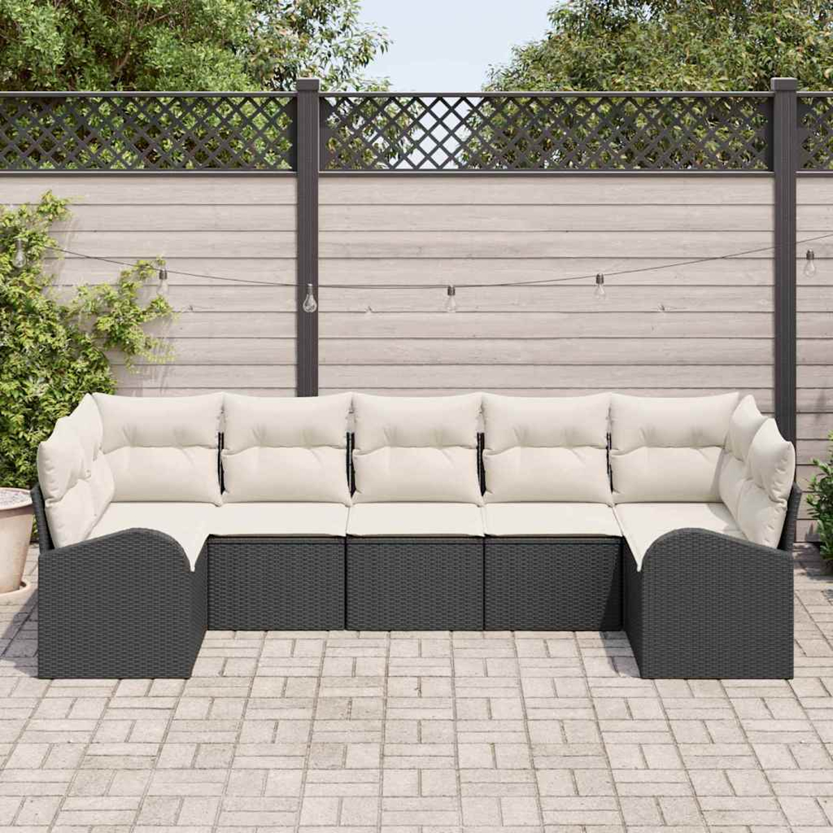 Ein modernes Outdoor-Ecksofa mit beigen Kissen und grauem Korbgeweberahmen steht auf einer gepflasterten Terrasse. Ein Holzzaun und Pflanzen sind im Hintergrund.