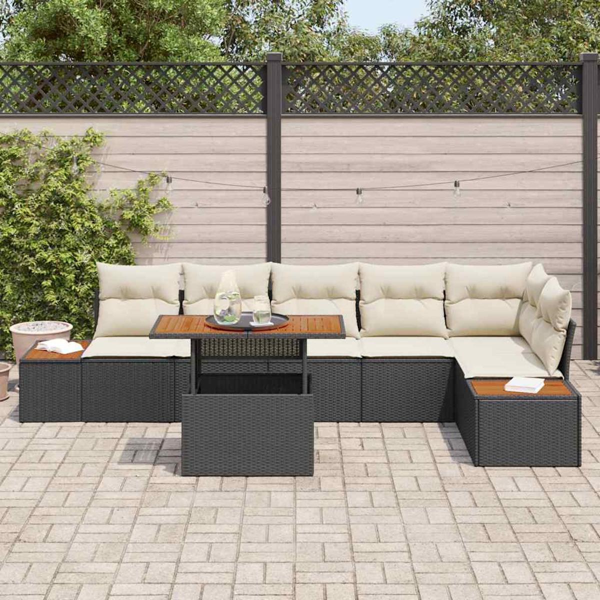 Outdoor-Ecksofa mit beigefarbenen Kissen und dunkelgrauem Korbgeflecht. Ein Holztisch hält Getränke. Hintergrund ist ein Zaun und Grün.