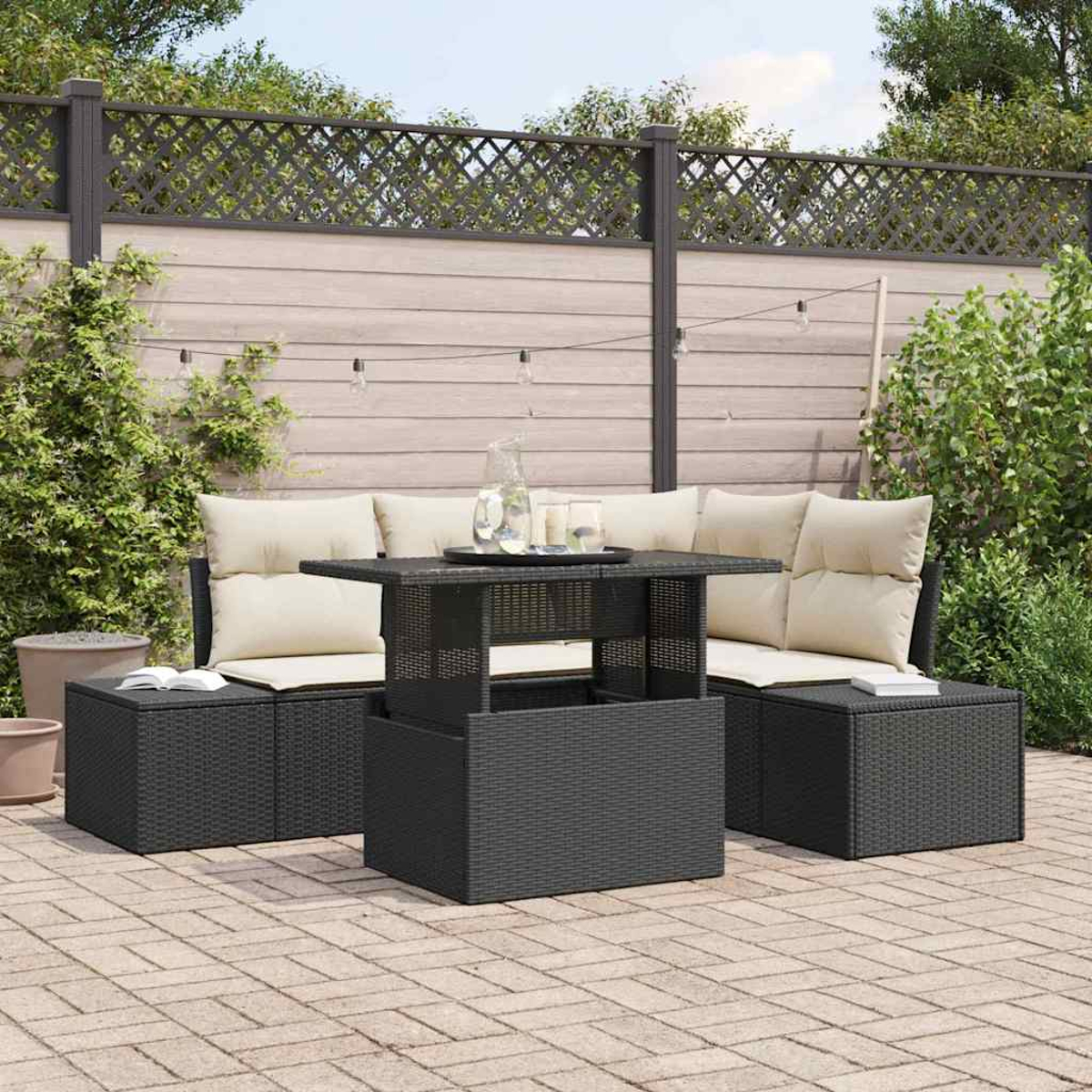Gartenmöbel-Set: schwarzes Rattan-Sofa, Tisch und Hocker mit cremefarbenen Kissen. Hinterhof mit Zaun und Pflanzen.