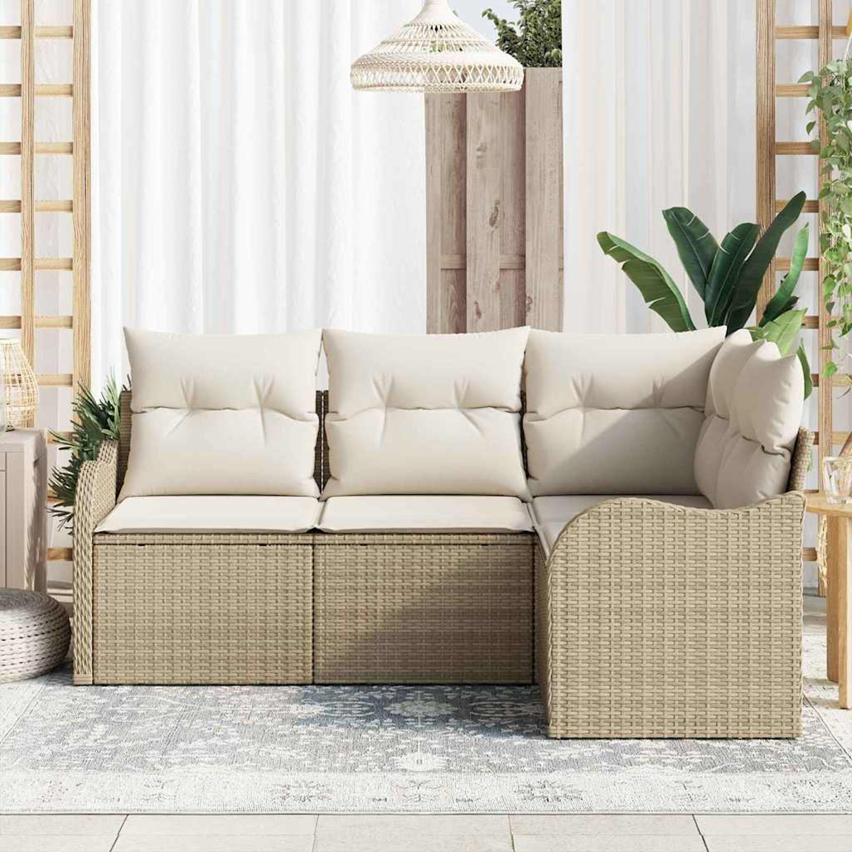 Geflochtenes Outdoor-Sofa mit cremefarbenen Kissen auf einem gemusterten Teppich. Hintergrund: weiße Vorhänge, Pflanzen und eine Hängelampe.