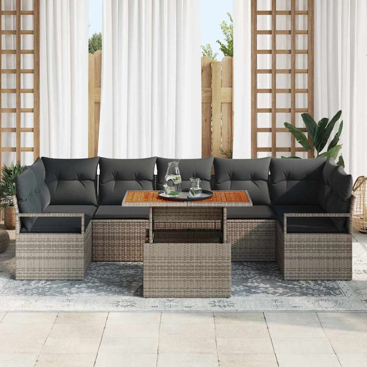 Outdoor-Ecksofa mit grauen Kissen und einem Holztisch, in der Nähe eines Fensters mit weißen Vorhängen. Pflanzen und ein Zaun sind sichtbar.