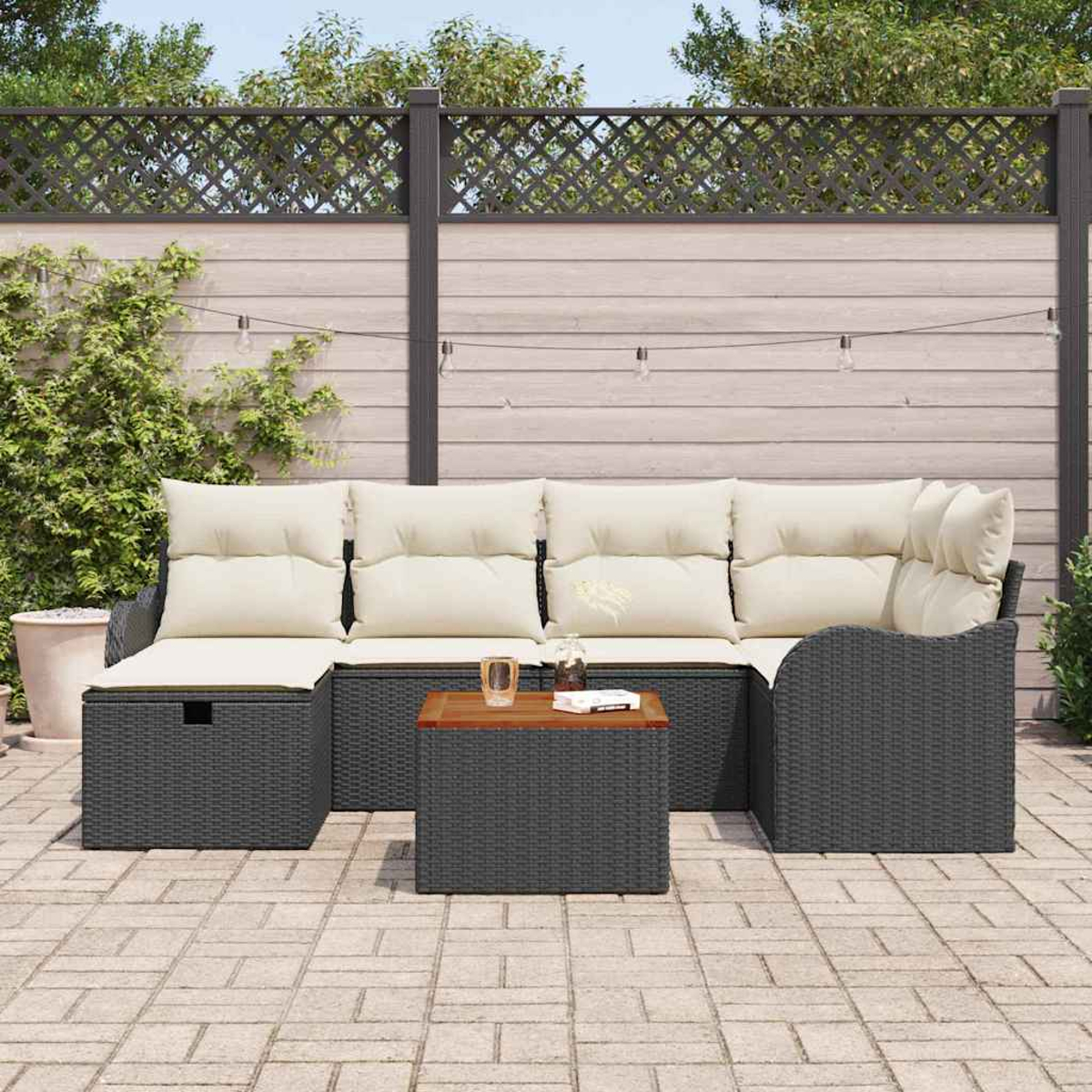 Garten-Sitzgruppe mit grauem Korbgeflecht, cremefarbenen Kissen und einem Holztisch. Auf einer Terrasse, mit Zaun und Pflanzen im Hintergrund.