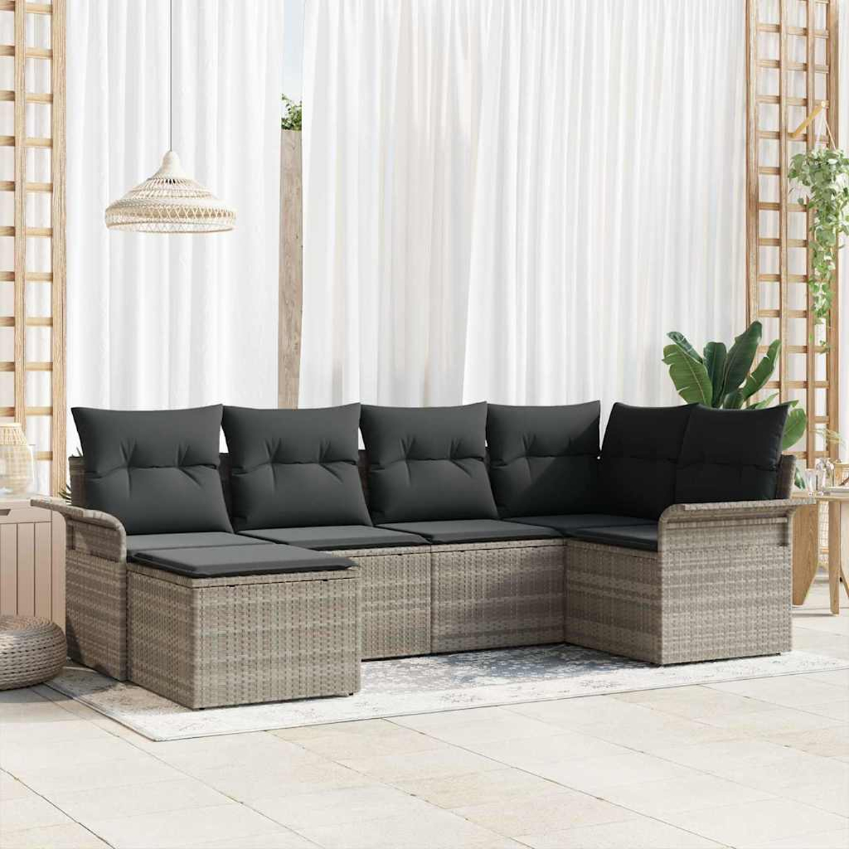 Ein Rattansofa mit dunkelgrauen Kissen steht auf einer Terrasse. Weiße Vorhänge und eine Hängelampe sind im Hintergrund.