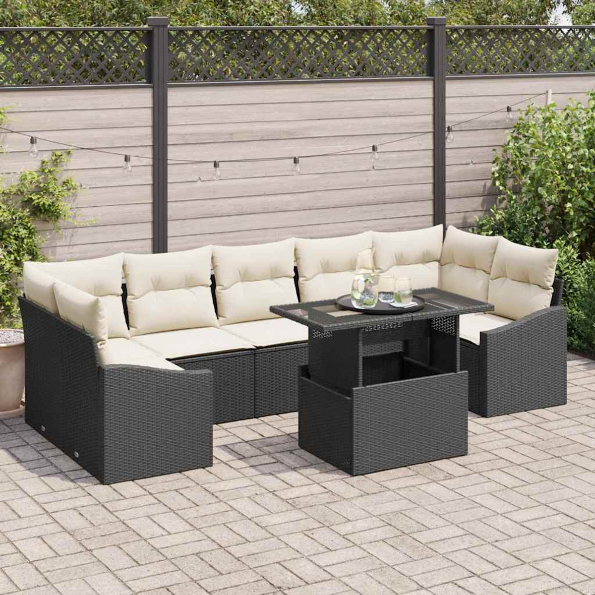 Outdoor-Sitzgruppe mit Kissen, einem Tisch mit Getränken und einer Kulisse aus Zaun und Grün auf einer Ziegelterrasse.
