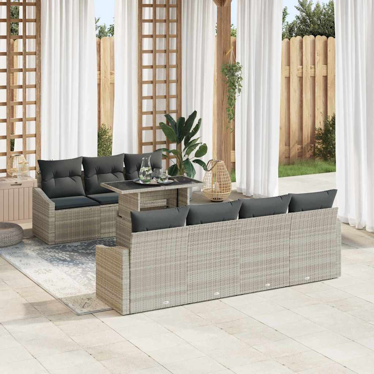 Gartenmöbel-Set. Graue Kissen auf gewebten Sofas und Tisch. Weiße Vorhänge und Holzzaun im Hintergrund sichtbar.