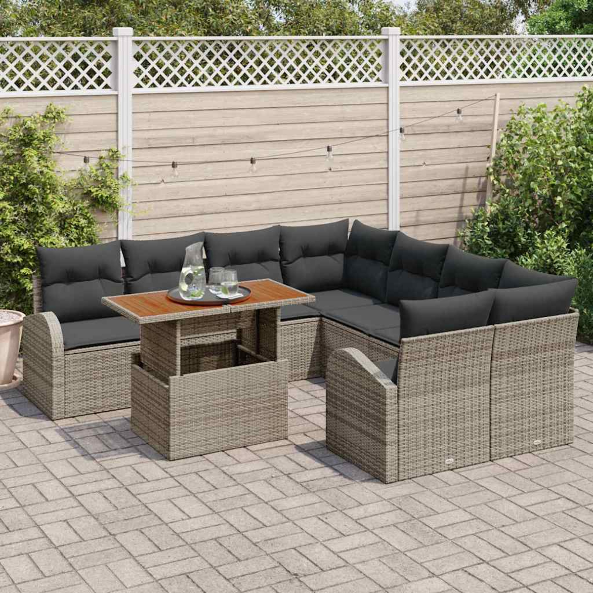 Rattansofa-Set im Freien mit grauen Kissen, einem Holztisch mit Getränken und einem Zaun im Hintergrund.