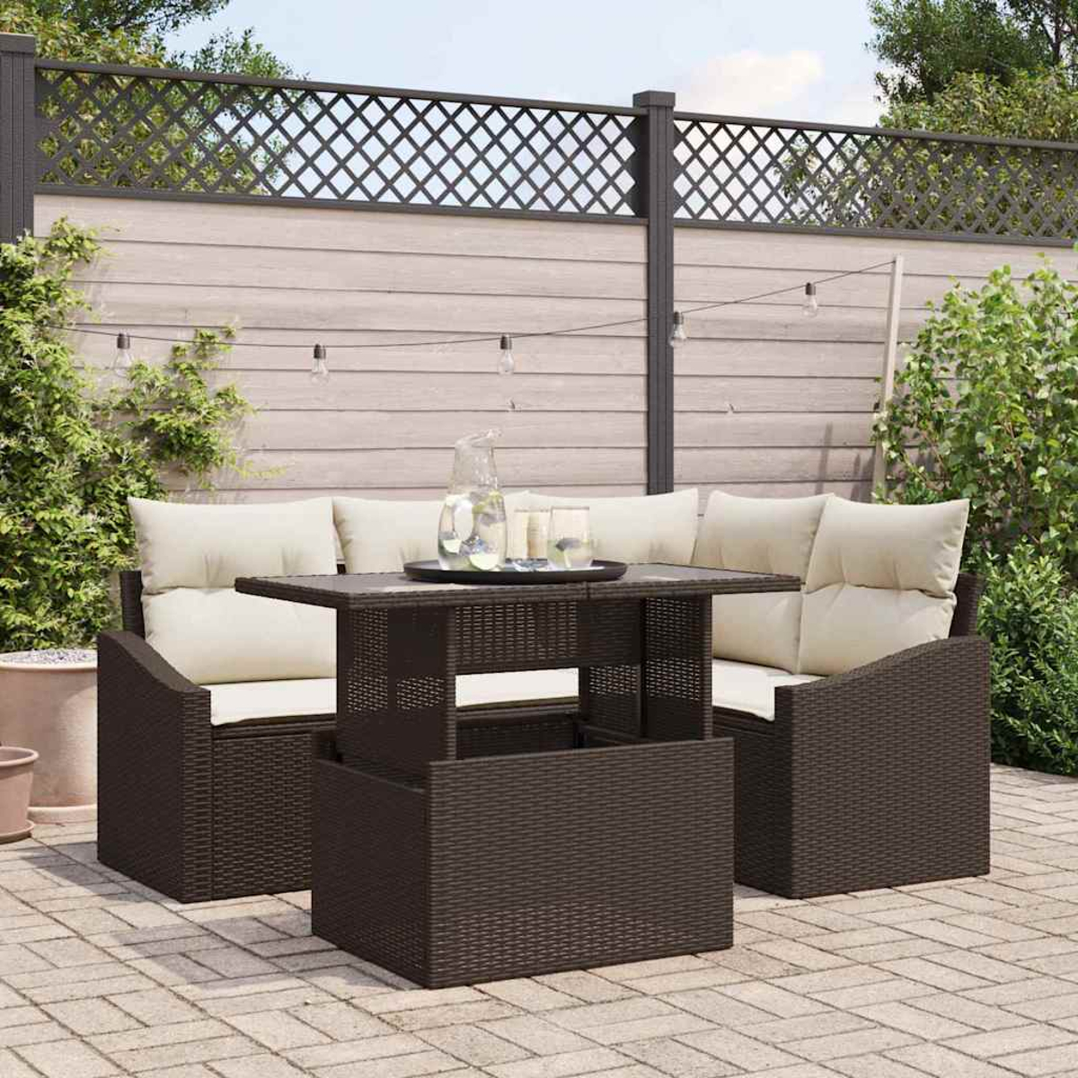 Garten-Terrassenset mit braunem Korbtisch und Stühlen. Beige Kissen, eine Glaskaraffe und Gläser stehen auf dem Tisch.