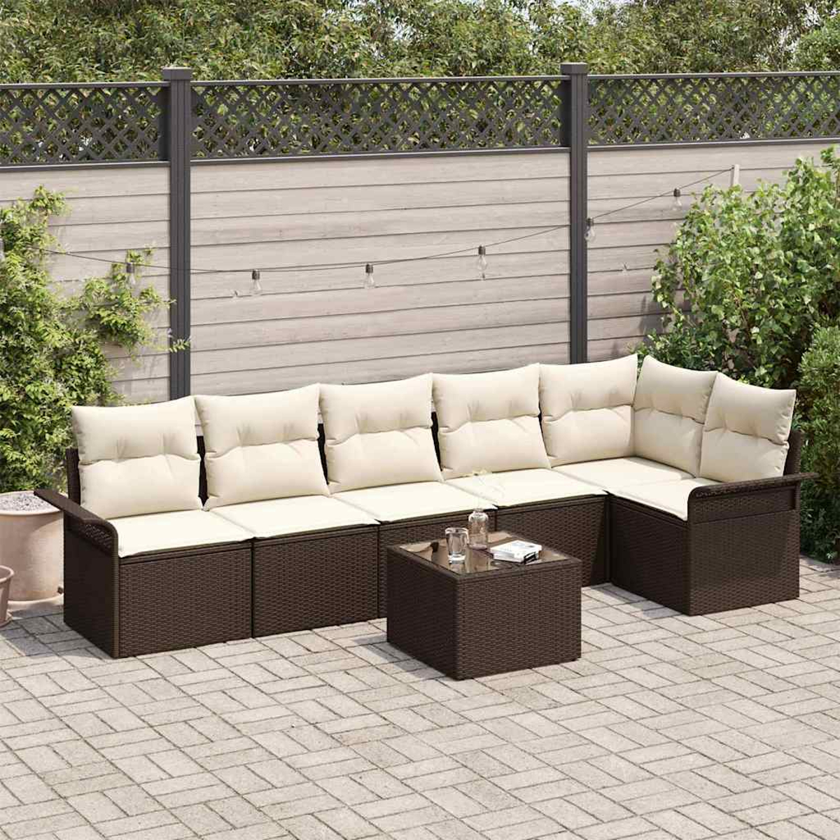 Ein Outdoor-Set mit braunen Korbmöbeln und cremefarbenen Kissen, einem kleinen Tisch und einem Zaun.