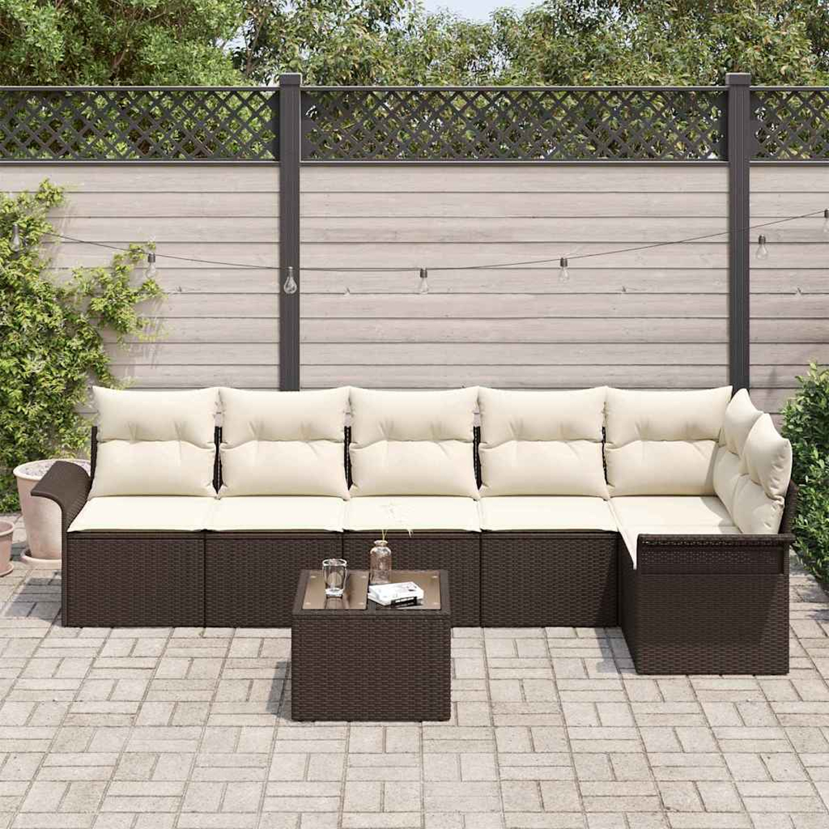 Outdoor-Ecksofa mit cremefarbenen Kissen und einem kleinen Tisch auf einer Terrasse. Im Hintergrund ein Holzzaun und Grün.