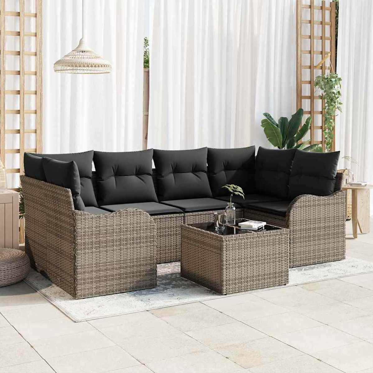 Garten-Terrassenset mit grauen Korbmöbeln, schwarzen Kissen und einem Couchtisch mit Glasplatte. Weiße Vorhänge und eine Hängelampe sind sichtbar.