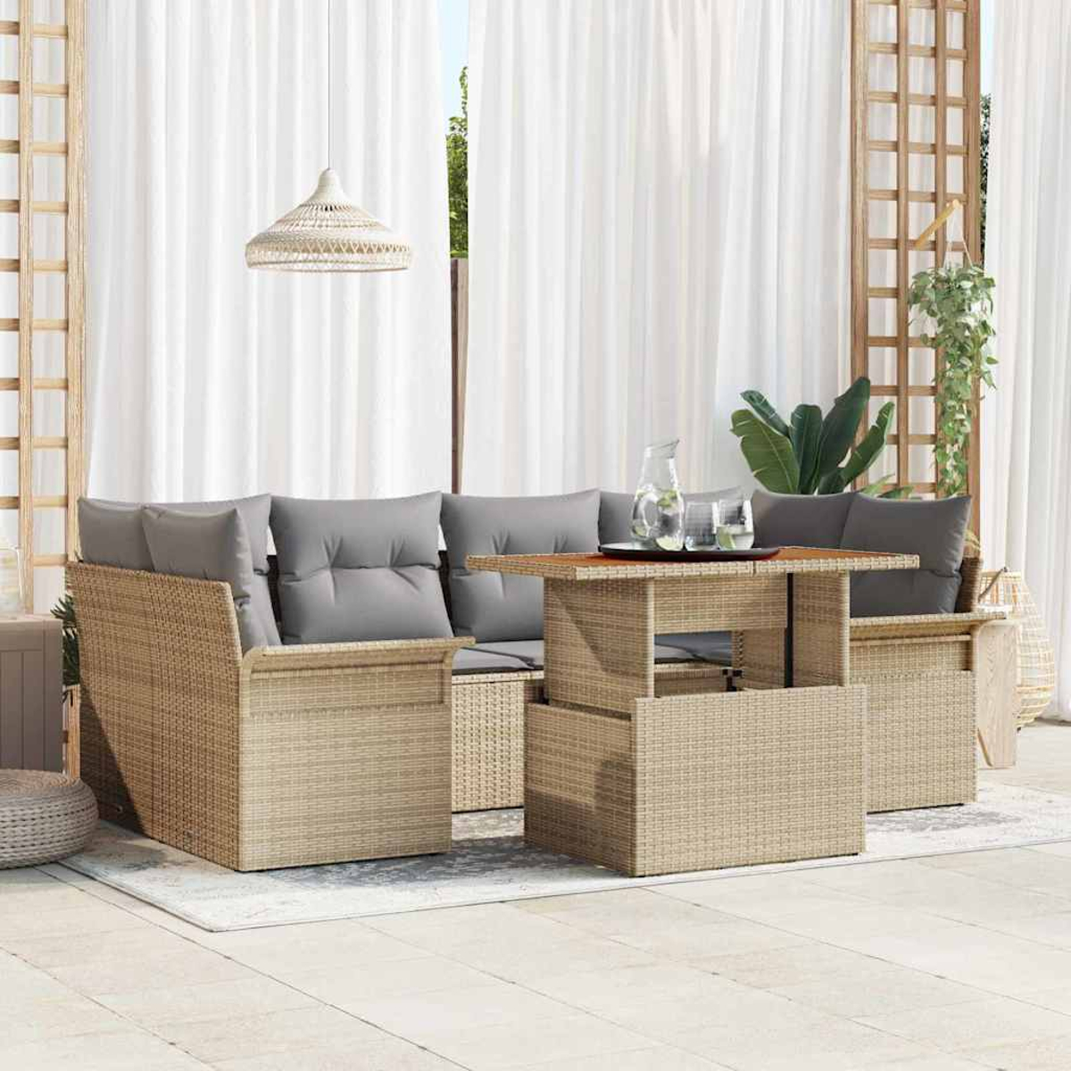 Gartenmöbel-Set aus Korbgeflecht mit grauen Kissen. Inklusive Tisch mit Gläsern und Krug, vor weißen Vorhängen.