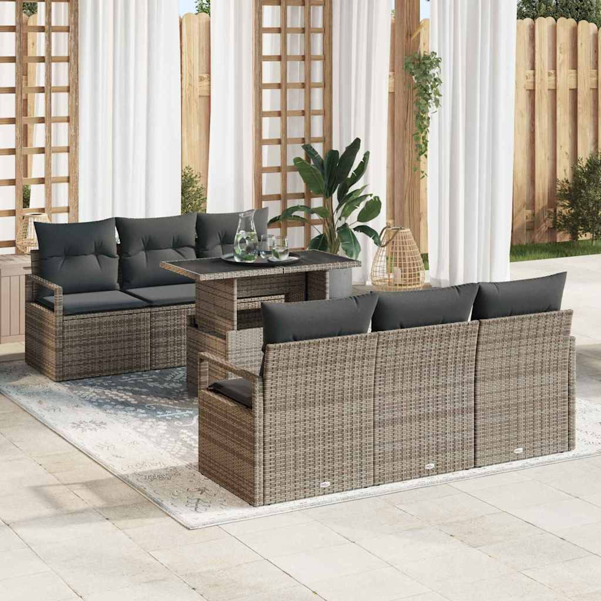 Terrassenset mit grauen Kissen, Korbmöbeln und einem Tisch. Weiße Vorhänge und Pflanzen im Hintergrund.