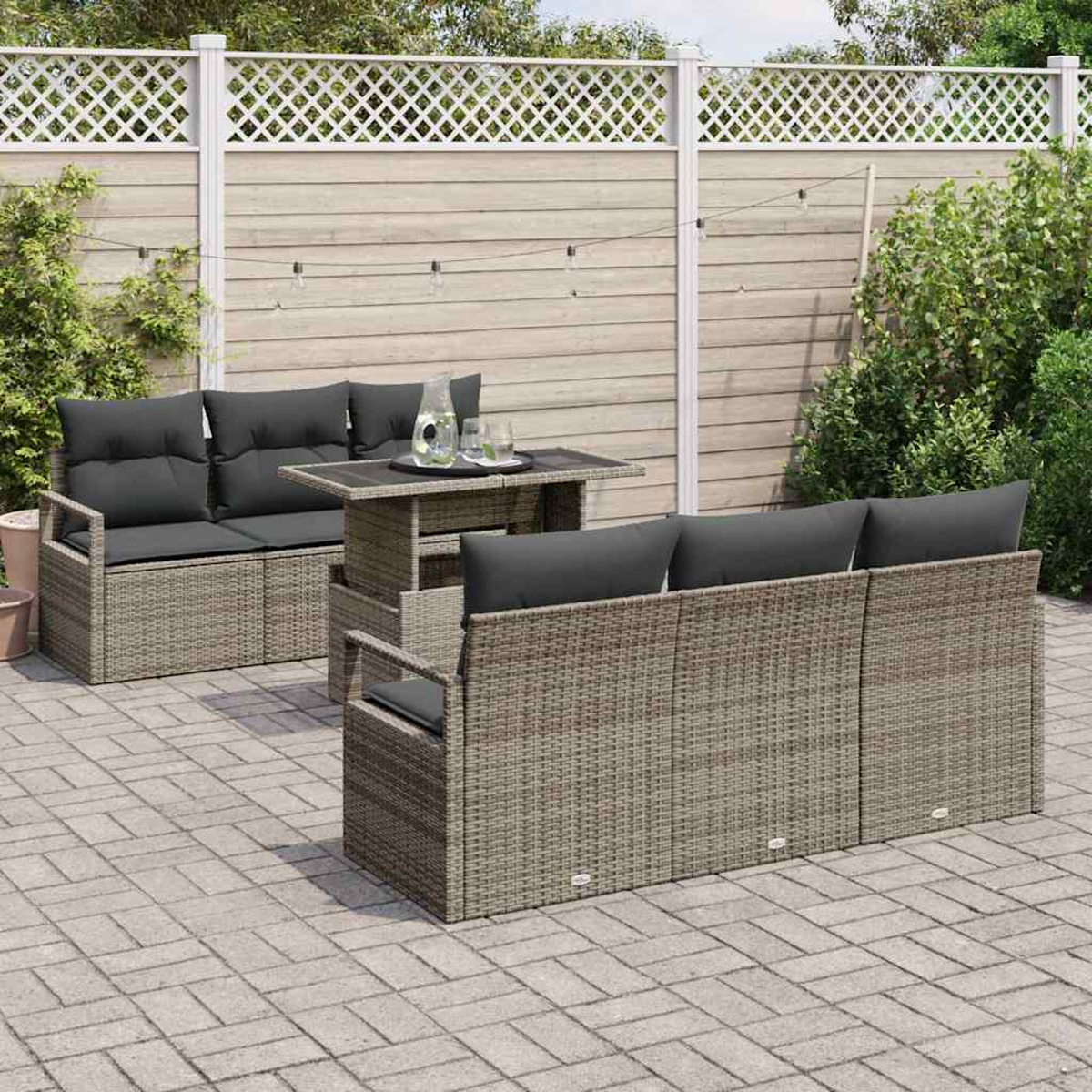 Garten-Terrassenset mit Korbmöbeln, grauen Kissen und einem Tisch. Ein weißer Gitterzaun und Grün bilden den Hintergrund.