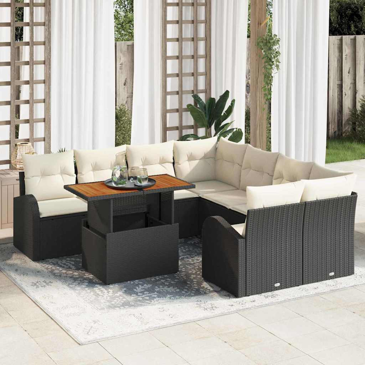 Juego de asientos al aire libre con estructura de mimbre negro, cojines beige y mesa de madera. Cortinas blancas y enrejado.